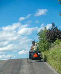 Obraz premium Amish man with a horse and cart cresting a hill on a country road | Holmes County, Ohio