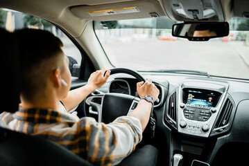 Young man with an earphone in his ear driving a car