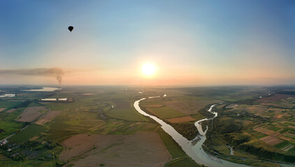 Aerial view of small hot air baloon flying over rural countryside at sunset