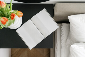 Open book and flowers on bedside table in bedroom interior