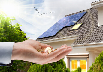 Hand with money against background of house with installed solar panels. Renewable energy and...