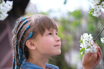 Naklejka premium Happy child girl playing in spring garden enjoying sweet scent of white cherry tree blossoming flowers on sunny day