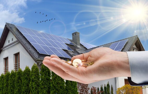 Solar panel on roof of  modern house and coins in hand. Concept of money saving and clean energy.
