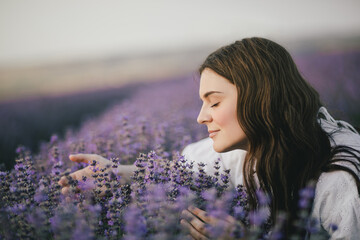 Young beautiful woman in white dress enjoying fragrance of lavender field.