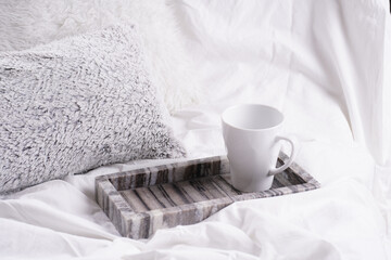 Fototapeta na wymiar an empty white porcelain cup for coffee or tea in grey marble tray on white bed sheets among fluffy pillows - breakfast in bed