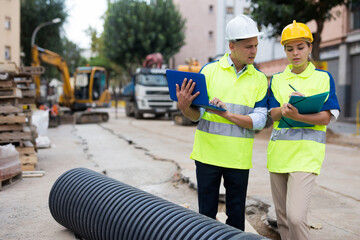 Male and female engineers standing in construction area and discussing. Man using laptop and woman holding folder in hands.