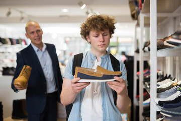 Portrait of interested teenager looking at two tone suede mens loafers while visiting shoe store