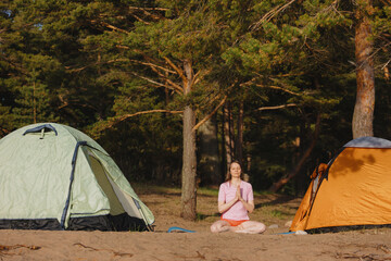 A woman meditates in front of a pine forest.