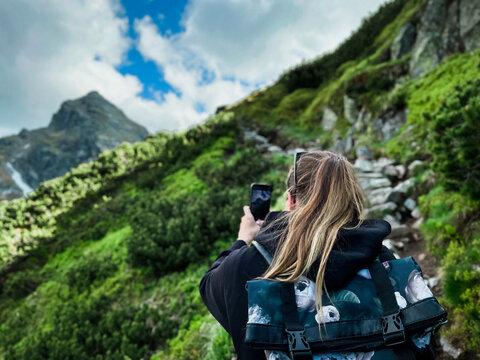 Young woman tourist with backpack taking photos on phone in mountains