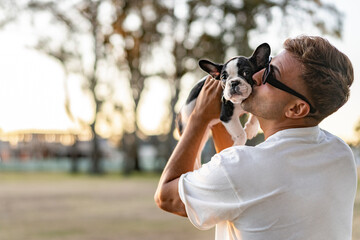 Happy man holding up and kissing a french bulldog.