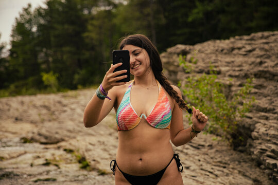 Brunette girl in bikini taking a photo with smartphone in the river