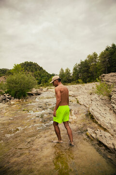 Dark-haired boy in a swimsuit walking in a river between mountains