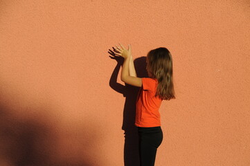 Cute little girl playing in shadow theater, making crocodile on orange color background. Child in black dress makes shadows outdoors.