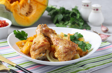 Baked chicken drumsticks with pumpkin and potatoes on white plate