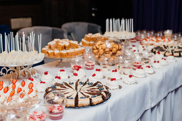 Candy bar. White wedding cake decorated by flowers standing of festive table with deserts, strawberry tartlet and cupcakes. Wedding. Reception Tartlets