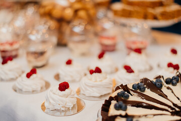Candy bar. White wedding cake decorated by flowers standing of festive table with deserts, strawberry tartlet and cupcakes. Wedding. Reception Tartlets
