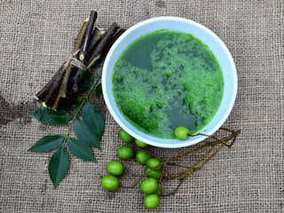 Neem leaves, fruits, and branches on jute fabric background. Neem medicinal herb juice in bowl....