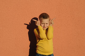 Boy playing in shadow theater, making crocodile on orange color background