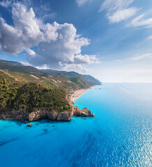 Aerial view of blue sea, mountain with green forest, rocks in water, sandy beach at sunset in summer. Lefkada island, Greece. Beautiful landscape with sea coast, azure water, sky with clouds. Top view