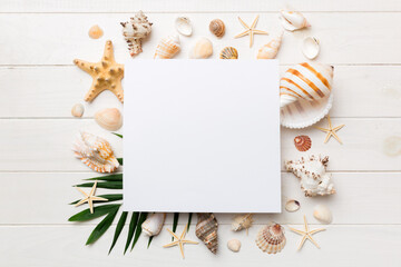 Summer time concept with blank greeting card and blank white paper on colored background. Seashells from ocean shore in the shape of frame separated with space for text top view