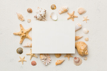 Obraz na płótnie Canvas Summer time concept with blank greeting card and blank white paper on colored background. Seashells from ocean shore in the shape of frame separated with space for text top view
