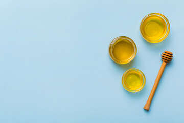 Glass jar of honey with wooden drizzler on colored background. Honey pot and dipper high above. Top view copy space