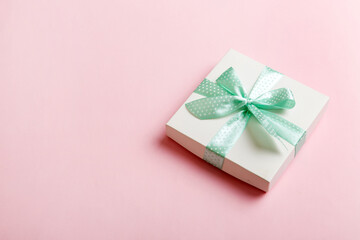 wrapped Christmas or other holiday handmade present in white paper with green ribbon on colored background. Present box, decoration of gift on colored table, top view with copy space