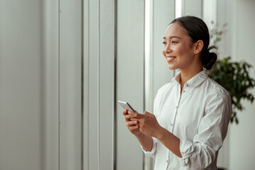 Asian business woman holding phone and looking window during break at office. High quality photo