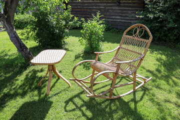 Rocking chair for recreation from rattan and small wicker table in summer garden on lawn in summer