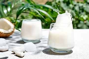 Coconut milk splash in drinking glass on palm leaf background. Vegetable milk, lactose free non...