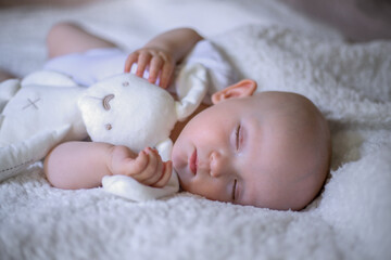 Sleeping baby in bed, holding a teddy bear.