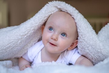 smiling baby looking at camera under a white blanket, towel.