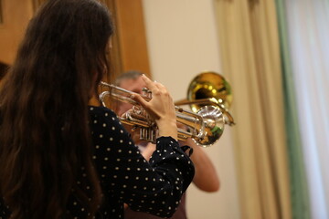 Woman playing a musical instrument holding a trumpet in her hands back view close-up focus on the details of the horn - obrazy, fototapety, plakaty