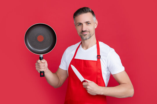 mature man chef smile in apron with frying pan and knife on red background