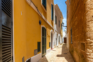 A long narrow alley street through the historic medieval center of Cuitadella de Menorca, Spain.