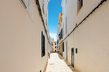 Fototapeta na wymiar A narrow whitewashed alley under a blue summer sky in the historic medieval center of Ciutadella de Menorca, Spain, on the Balearic island of Menorca in the Mediterranean Sea