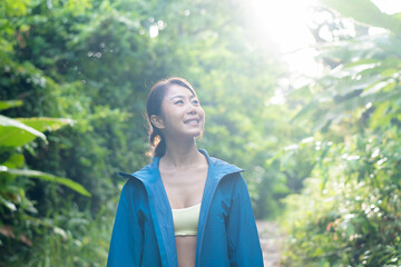 Young female explorer smiling and hiking in the forest mountain trail. Asian woman walking outdoors.