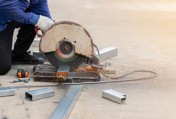 Worker cutting steel bar by circular saw in​ the​ factory area.