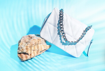 Female bag with iron chain and the shadow of a tropical leaf on blue background.