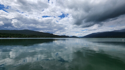 Whitefish Lake in Flathead County, Montana under dramatic summer cloudscape reflected in calm water of lake.