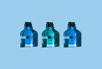 Three different perfume bottles on a pastel blue background in the sunlight. Flat lay, top view....