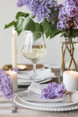 Beautiful table decor for a wedding dinner with a spring blooming lilac flowers. Celebration of a special event. Fancy white plates, wineglasses, candles. Countryside style