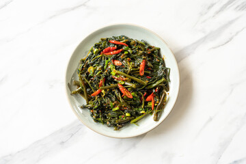 Stir-fried water spinach is photographed flat lay on a ceramic table.