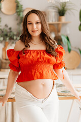 a pregnant woman in a romantic orange blouse and trousers in white interior 