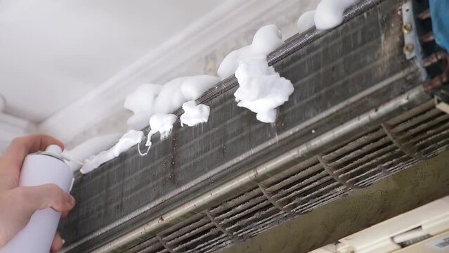A man sprays special foam to clean air conditioners on the radiator. Split system maintenance.