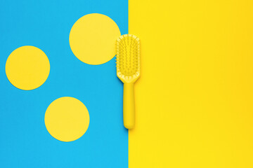 Yellow comb made of plastic on an abstract yellow-blue background. Minimal hair care concept.