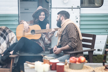 Young beautiful loving couple travelling across country in the van. Millennial man and woman in a travel camper. Cozy atmosphere, vacations vibe. Playing guitar, drinking tea, cooking on a campfire
