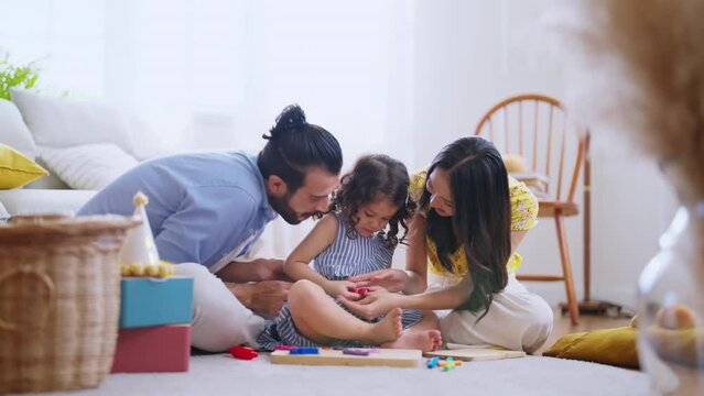 Happiness Family sitting in casual living room playing moulds from plasticine at home, Girl daughter sculpt figures from soft colorful  Clay Dough with her parents with joyful smile watching takecare