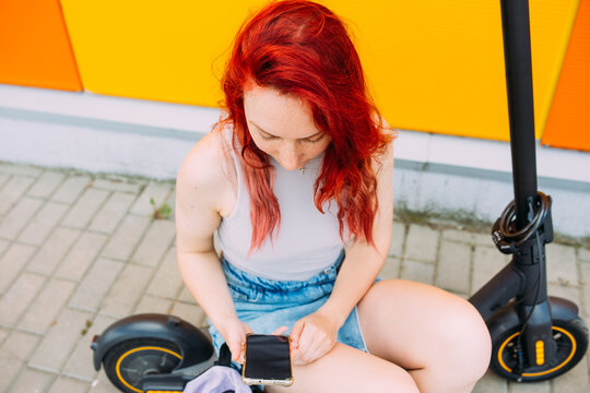 Woman uses a smartphone and an electric scooter in the summer in the city
