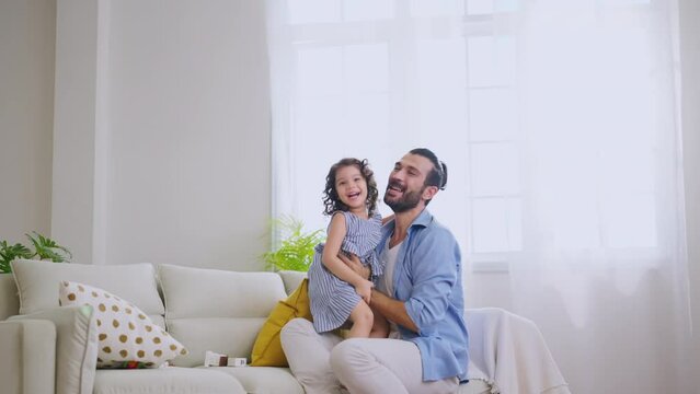 Happiness dad playing hug flying plane with girl daughter joy fun and exited in living room at home,father holding girl child flying around on sofa with love care tenderness and adorable moment